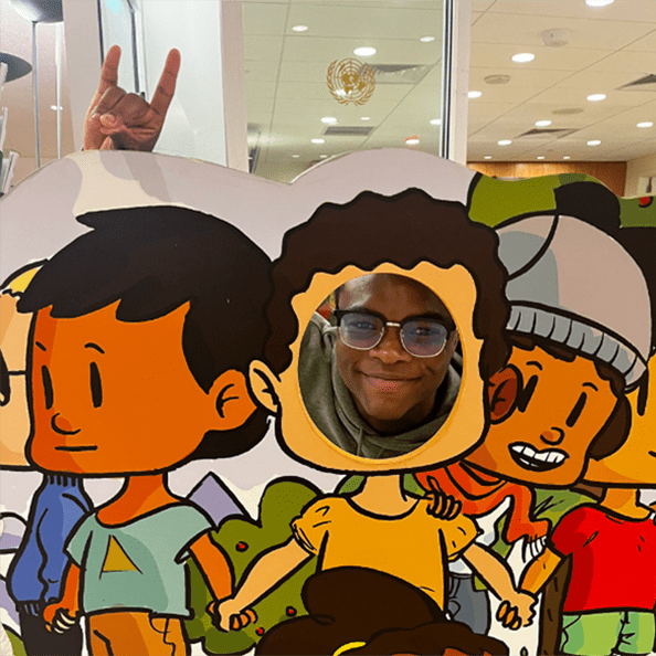 Fairfield student taking a photo with the 'Stags Up' hand gesture with their head in a cardboard cutout photo op area.